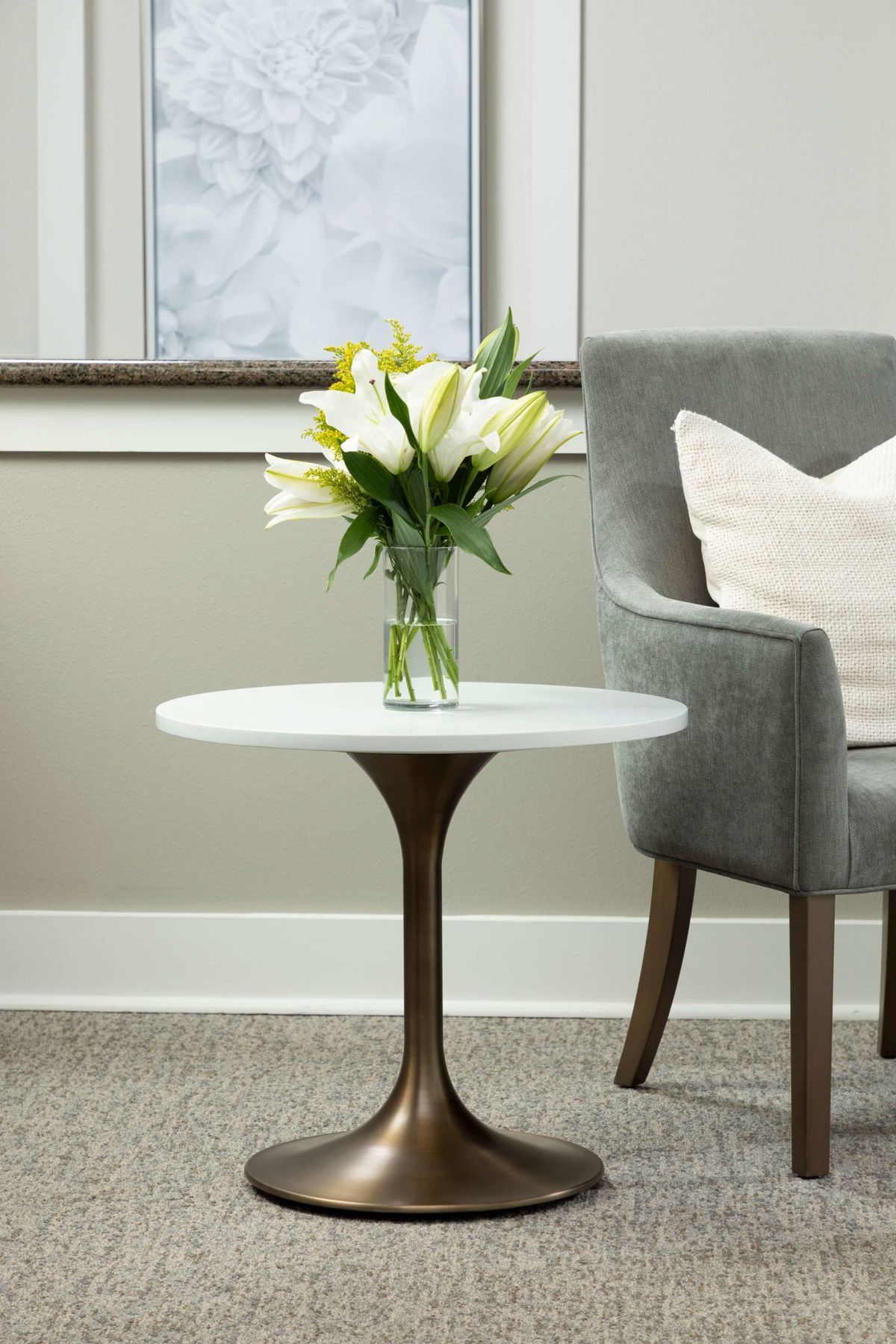 A cozy living room corner with a small round table holding a vase of flowers next to a plush chair.
