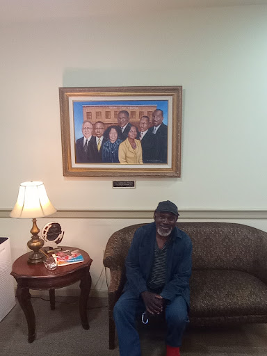 A man sitting on a couch in a room with a portrait of a group of people hanging on the wall.