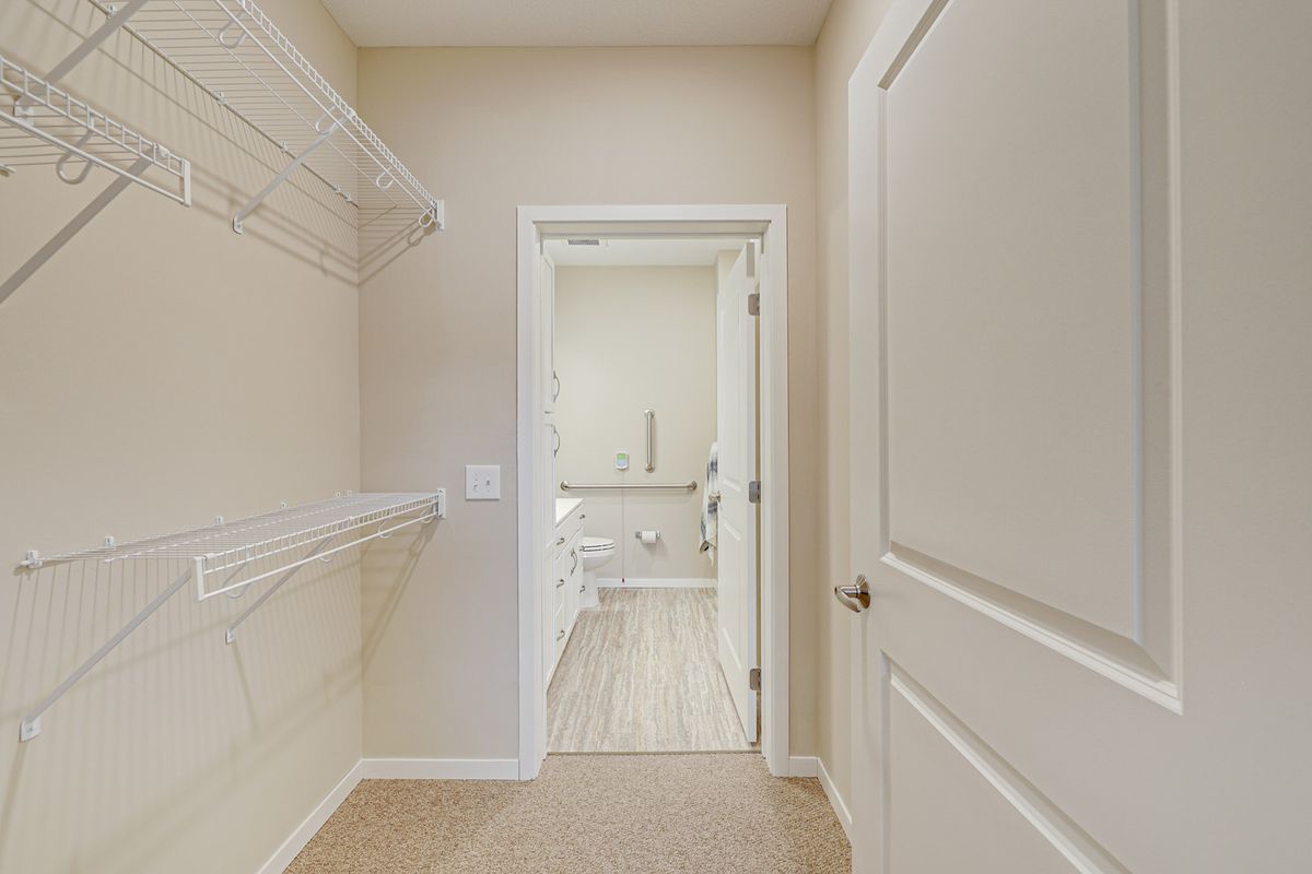 An empty walk-in closet with shelving leading to a bathroom.