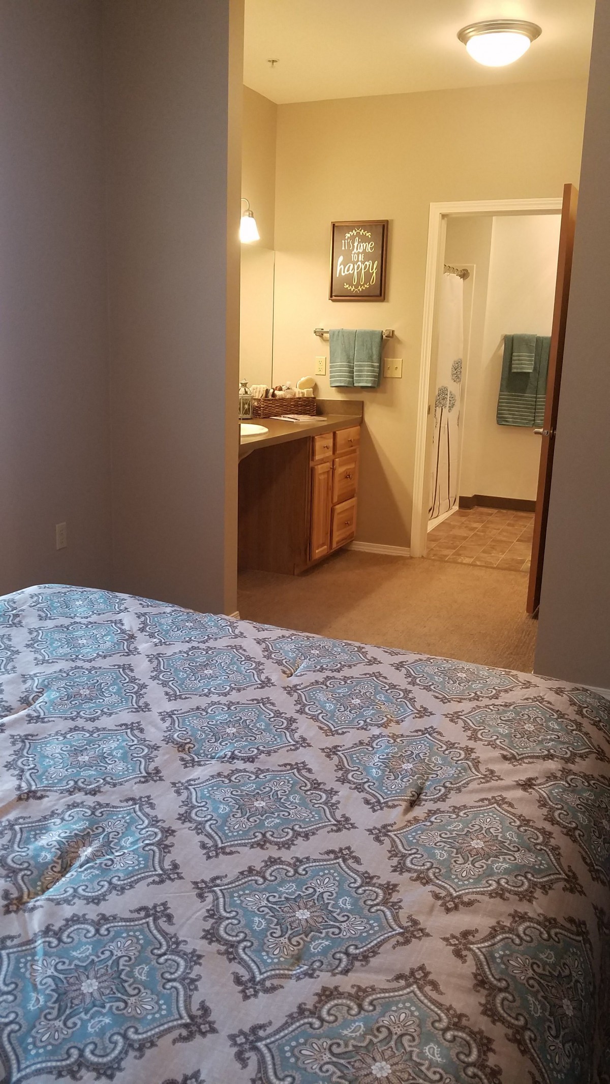 A cozy bedroom with a view of an adjoining bathroom, featuring elegant bedding and neatly hung towels.