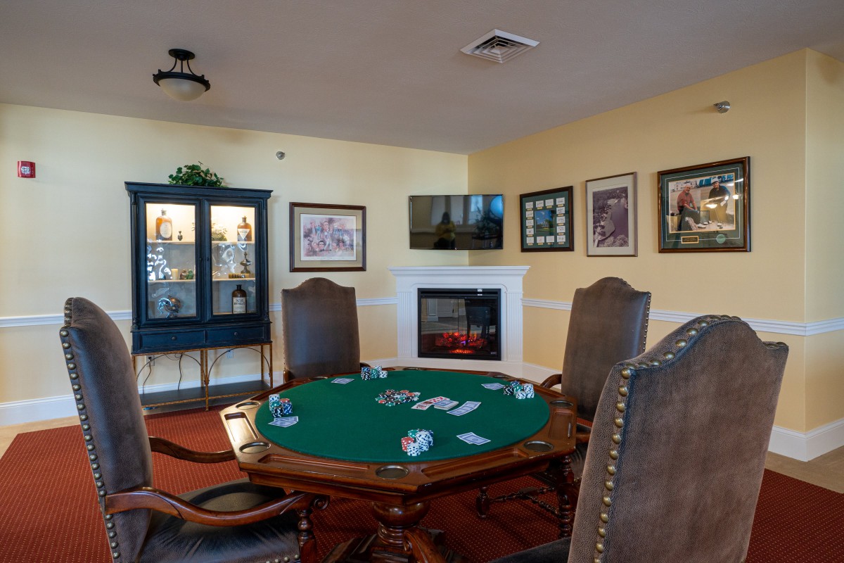 A cozy game room featuring a poker table with cards, surrounded by leather chairs and decorated with framed artwork and a fireplace.