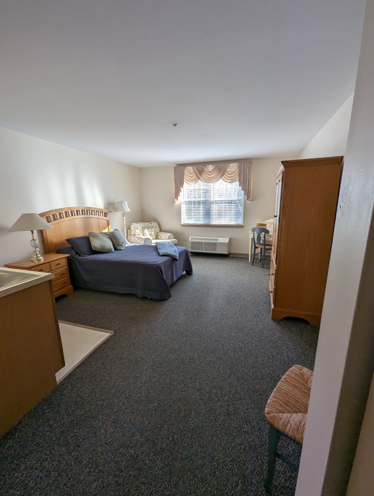A cozy bedroom with a bed, nightstands, and an armchair near the window.