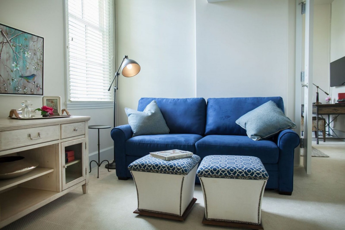 A cozy living room with a blue sofa, stylish ottomans, and soft lighting.