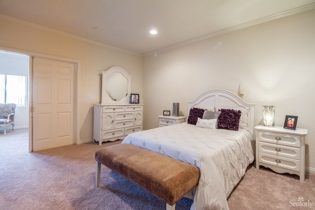 A cozy bedroom with a neatly made bed, white dresser with a mirror, and decor accents.