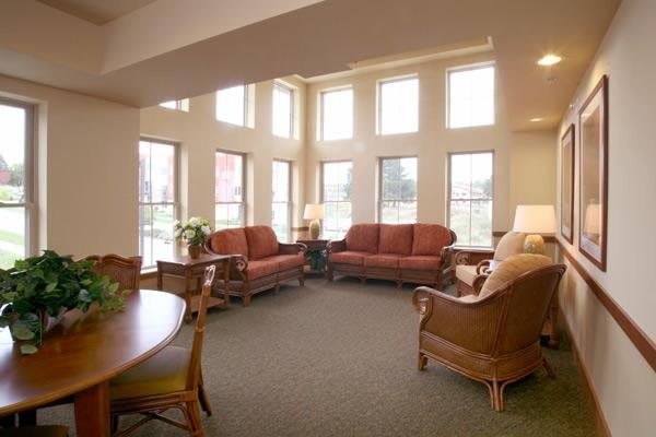 A spacious living room with ample natural light, featuring multiple sofas and large windows.