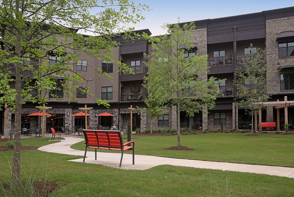 A modern apartment building with a well-maintained outdoor area featuring benches and lush greenery.