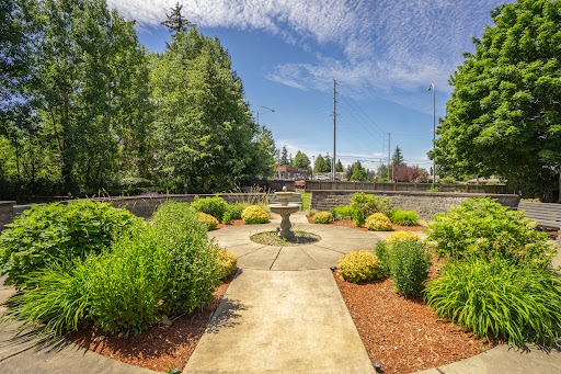 A serene garden space featuring a central fountain, surrounded by lush greenery and a clear blue sky.