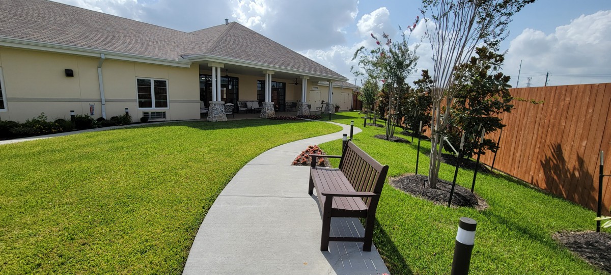 A peaceful backyard scene featuring a walkway, bench, and well-maintained lawn.