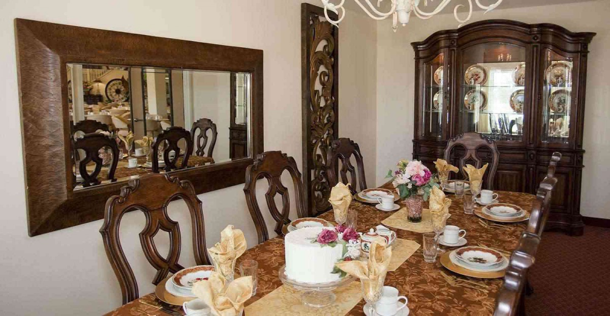 An elegant dining room setup with a beautifully arranged table featuring ornate wooden chairs, a mirror on the wall, and a chandelier overhead.