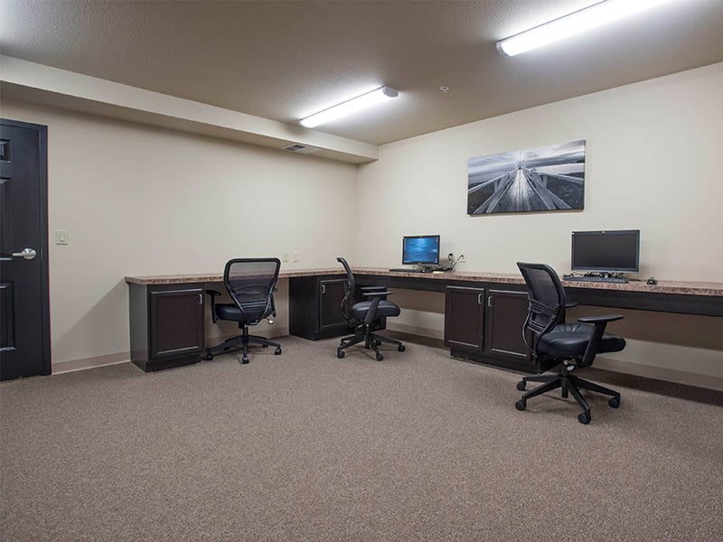 An empty office space with desks, chairs, and computers under fluorescent lighting.