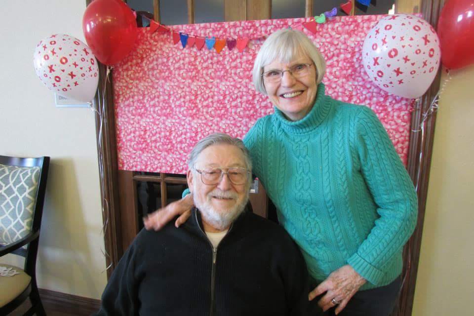 A smiling couple poses together in front of a festive background with balloons.