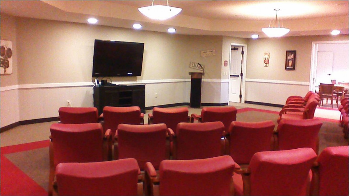 A small conference room with red chairs, a television, and a podium.