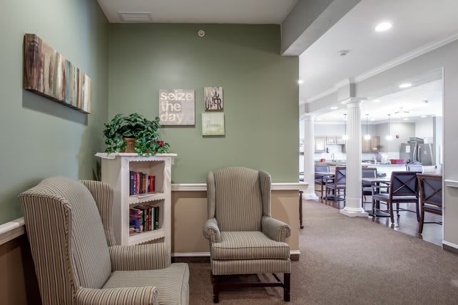 A cozy interior space with two armchairs, a small bookshelf, and wall art against a green-painted wall.