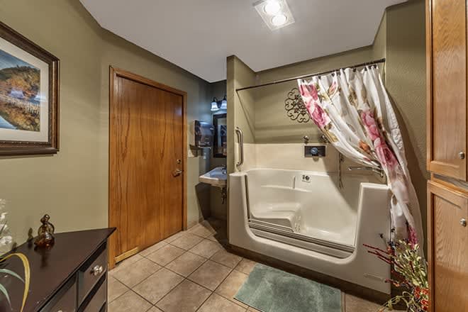 A bathroom with a walk-in tub, tiled floor, and wooden door.