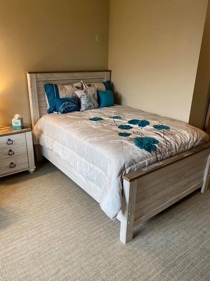 A cozy bedroom featuring a bed with floral bedding, a bedside table, and a lamp.