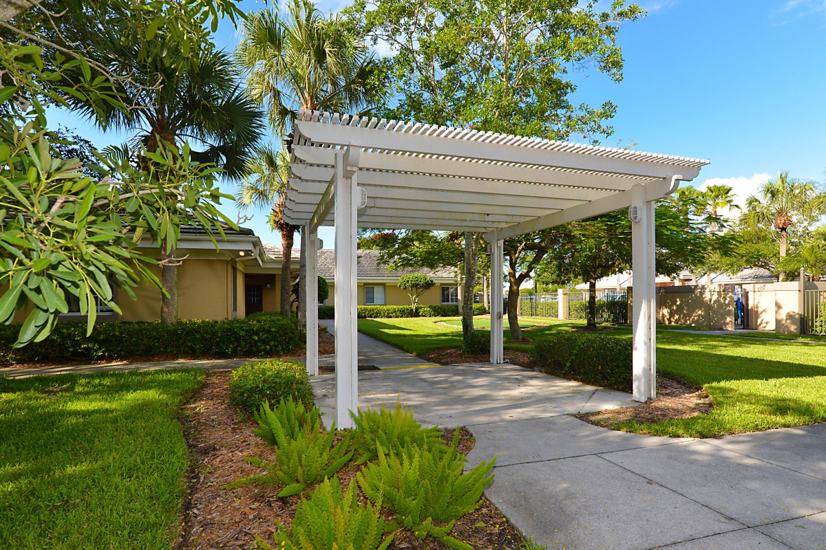 A white pergola over a garden walkway surrounded by lush greenery and trees.