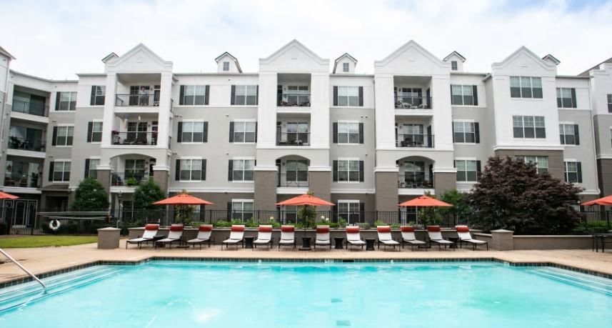An apartment complex with a pool and lounging area.