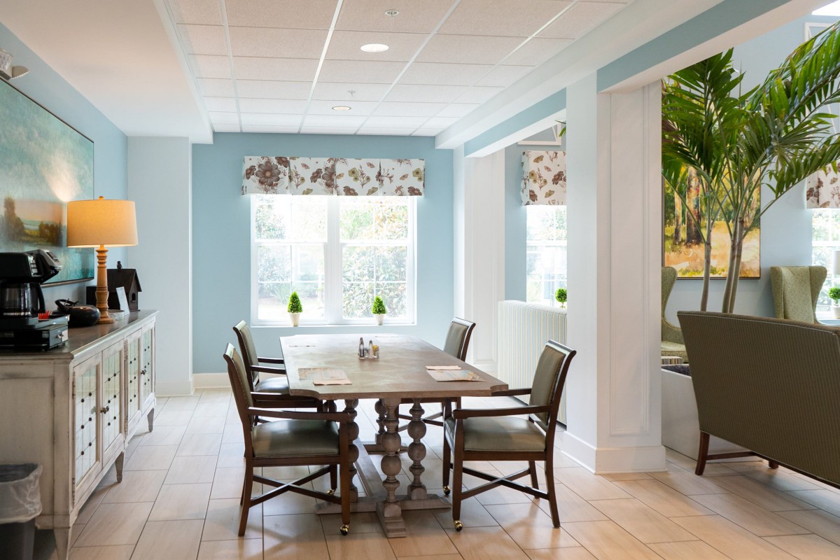 A bright dining area with a wooden table, surrounded by chairs and adorned with floral window treatments.