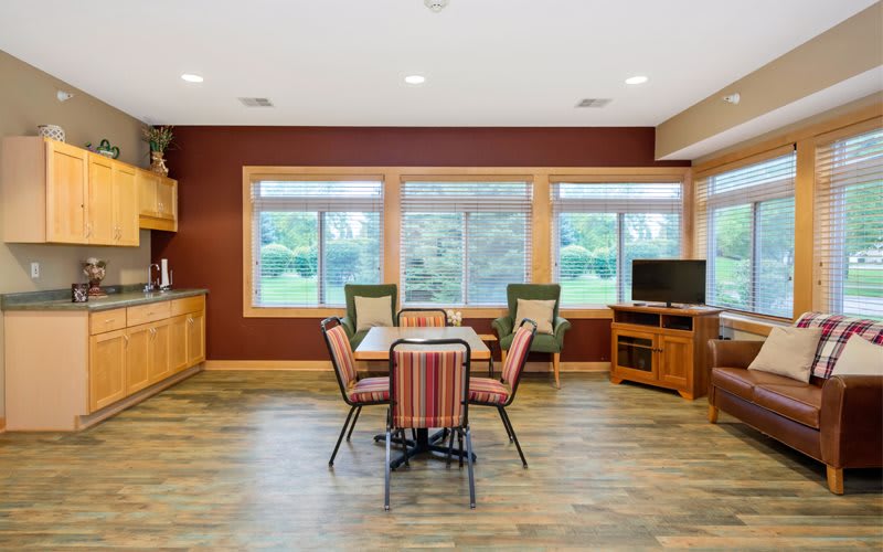 A cozy dining and living room space with large windows, comfortable seating, and a television.