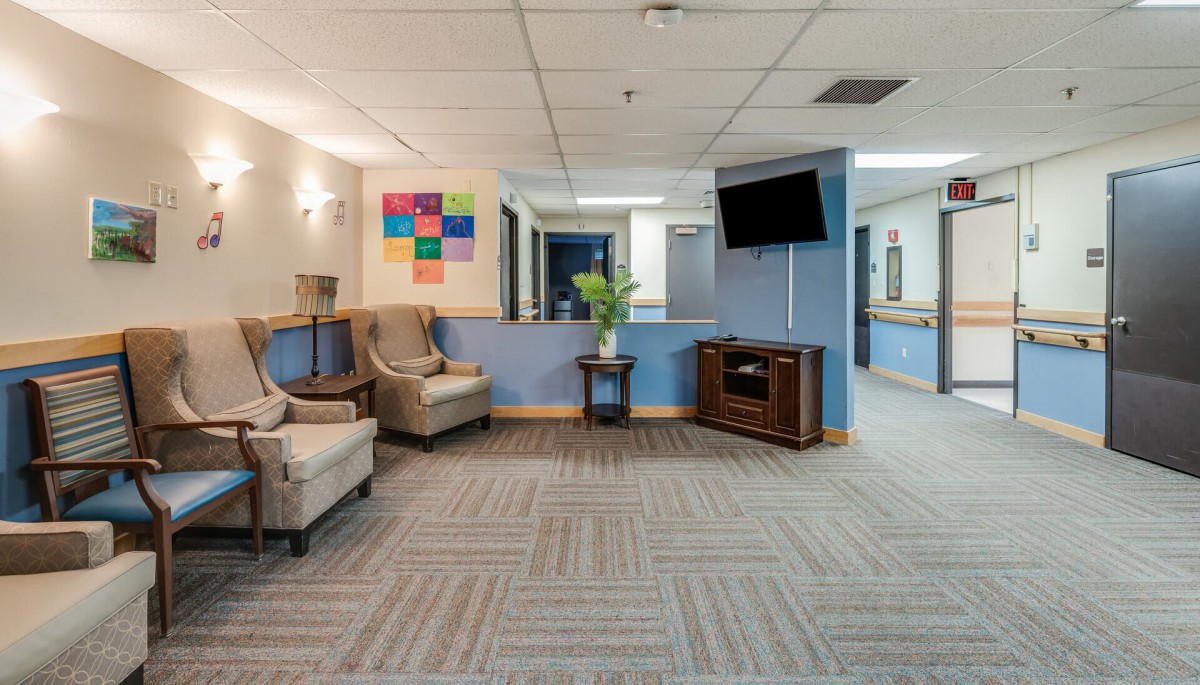 A modern waiting room with comfortable seating, a television mounted on the wall, and vibrant artwork displayed above a side table.