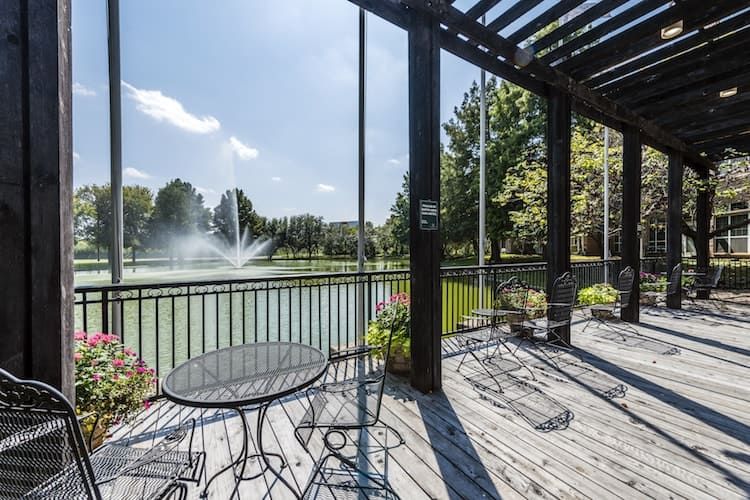 A peaceful patio overlooking a lake with a fountain under a clear blue sky.