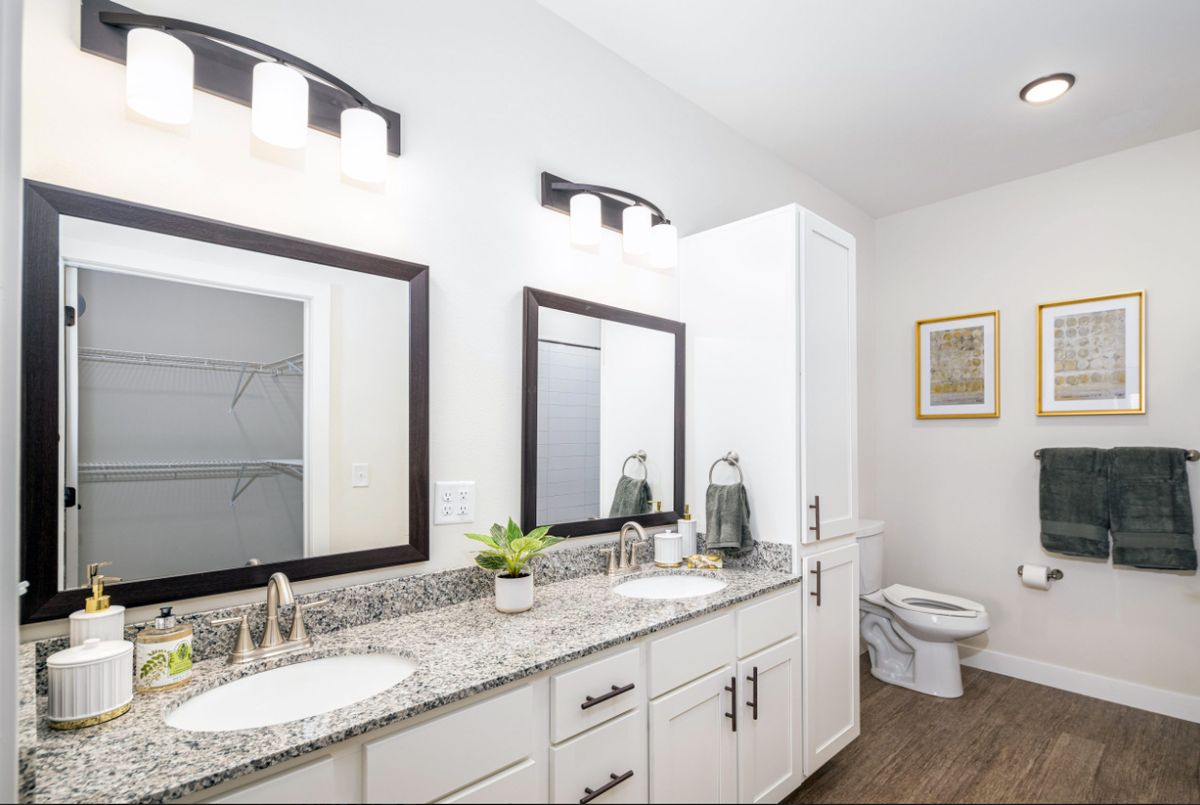 A modern bathroom with double sinks and granite countertops, featuring white cabinets and sleek light fixtures.