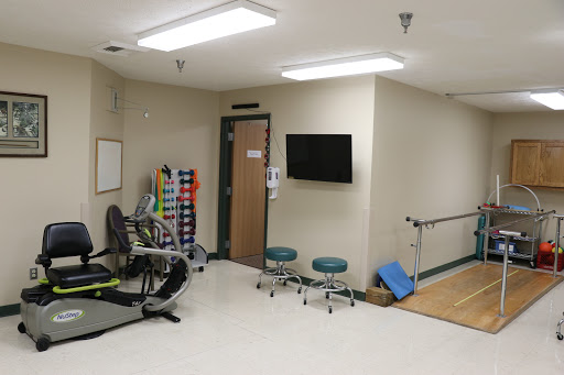 A well-equipped physical therapy room featuring exercise equipment, chairs, and a TV for patient use.