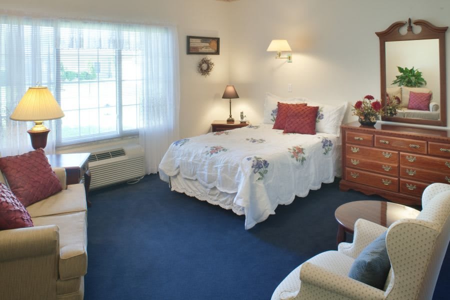 A cozy bedroom with a neatly made bed, decorated with floral patterns and soft lighting.