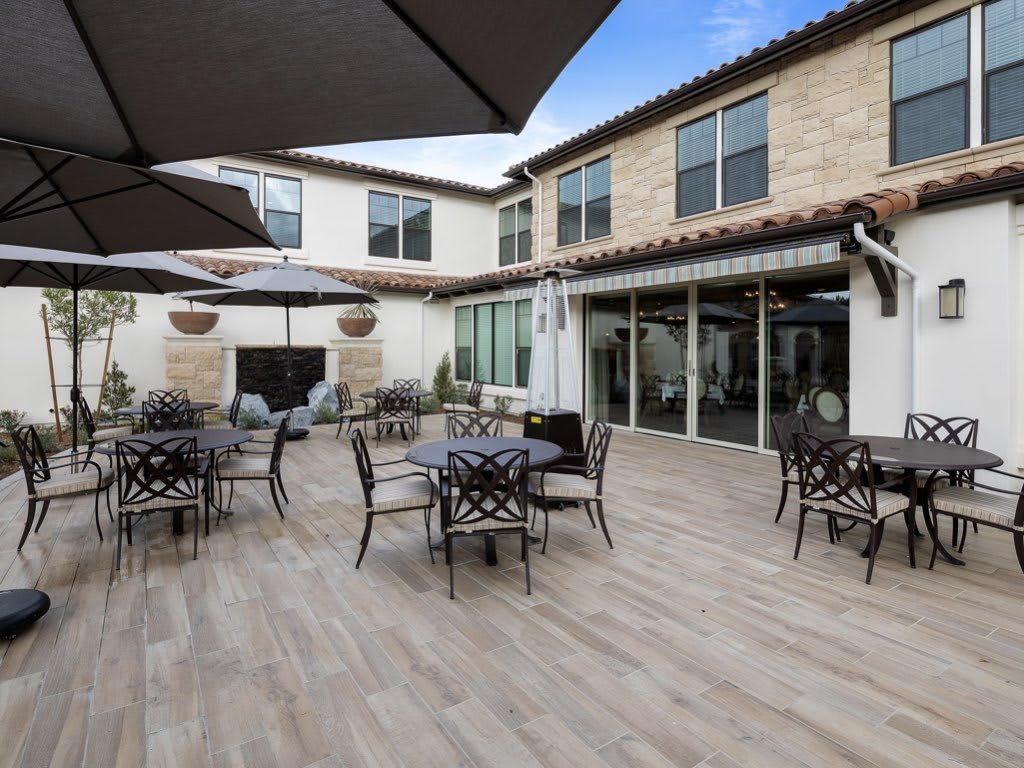 A spacious outdoor patio area with tables, chairs, and large umbrellas, set against the backdrop of a building with a stone facade.