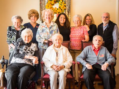 A group of elderly people and caregivers smiling together indoors.