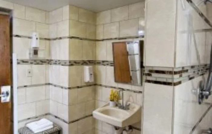 A tiled bathroom with a small sink, mirror, and soap dispenser.