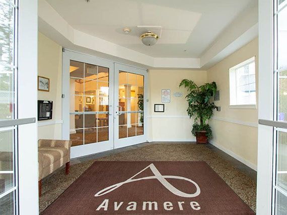 The image shows the entrance to a lobby area with glass doors, a welcome mat, and a potted plant.