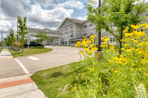 A serene view of a residential building surrounded by vibrant flowers and lush greenery under a cloudy sky.