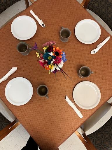 An elegant table set for a meal, featuring white plates, brown cups, and a vibrant floral centerpiece.