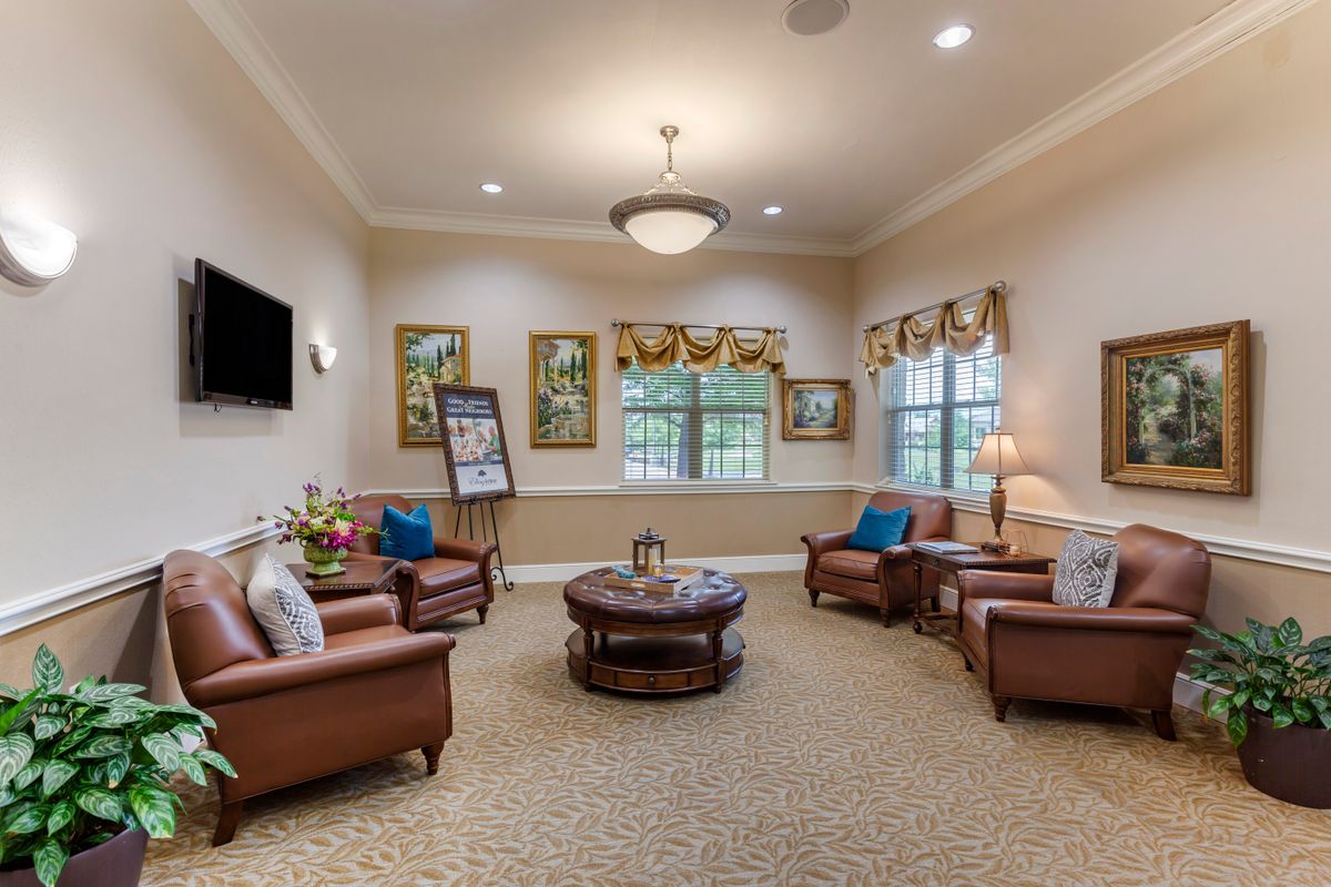 A cozy living room with several armchairs and a coffee table, decorated with artwork and large windows.