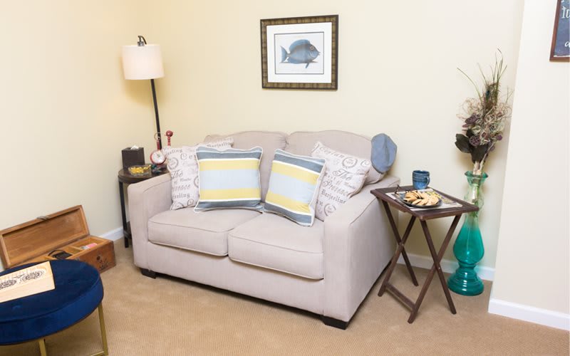A cozy living room corner with a beige sofa and striped cushions, accompanied by a side table and a standing lamp.