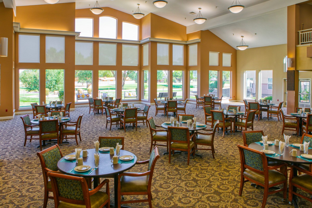 A spacious dining room with large windows, elegant tables and chairs, and bright lighting.