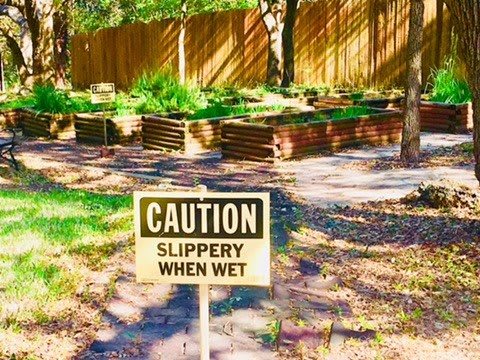 A caution sign warning 'Slippery When Wet' placed in a garden area.