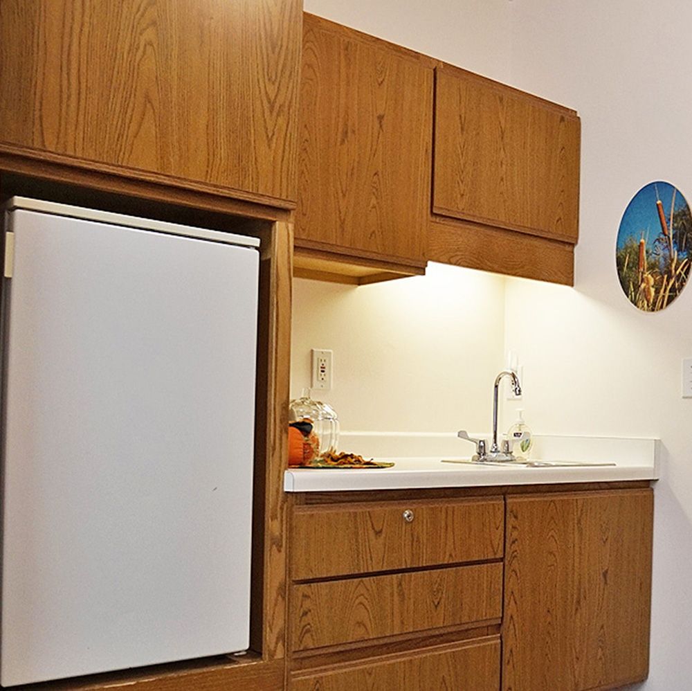 A minimalist kitchen setup with wooden cabinets, a sink, and a small fridge.