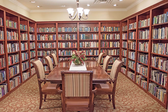An elegant library with shelves filled with books and a central table surrounded by chairs.