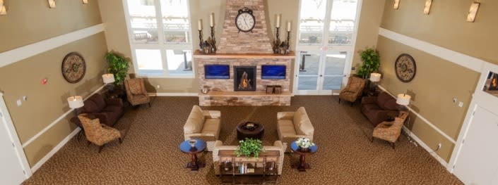 A cozy living room with a central seating area, featuring armchairs and tables around a fireplace with a clock above it.