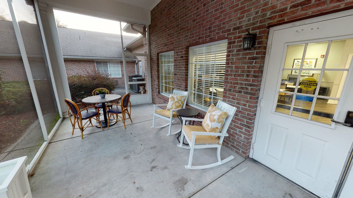 A cozy patio area featuring rocking chairs and a table set against a brick wall.
