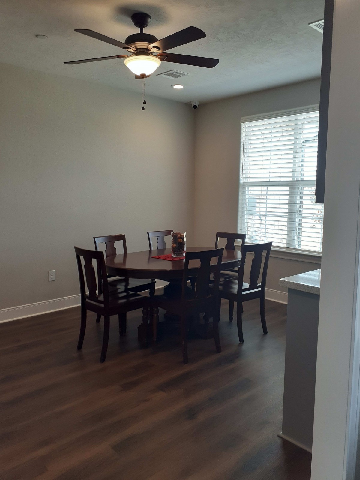 A cozy dining area with a round wooden table and four chairs, featuring natural light from a window with blinds.