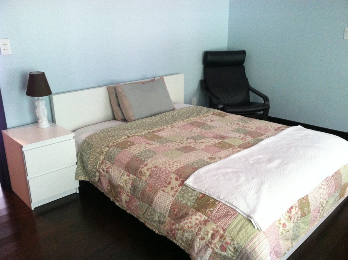 A cozy bedroom with a bed, chair, and bedside table featuring a lamp.