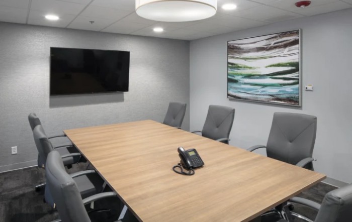 A modern conference room with a large meeting table, chairs, and a TV screen.