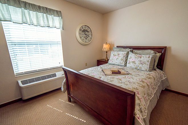 A cozy bedroom with a wooden bed frame, floral bedding, and a bedside lamp.