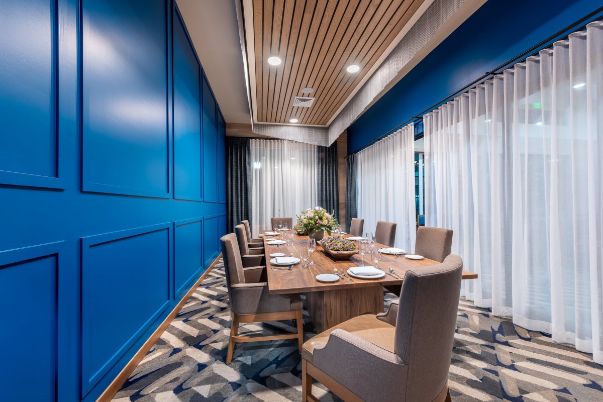 A modern dining room with blue walls, a wooden table, and comfortable chairs.