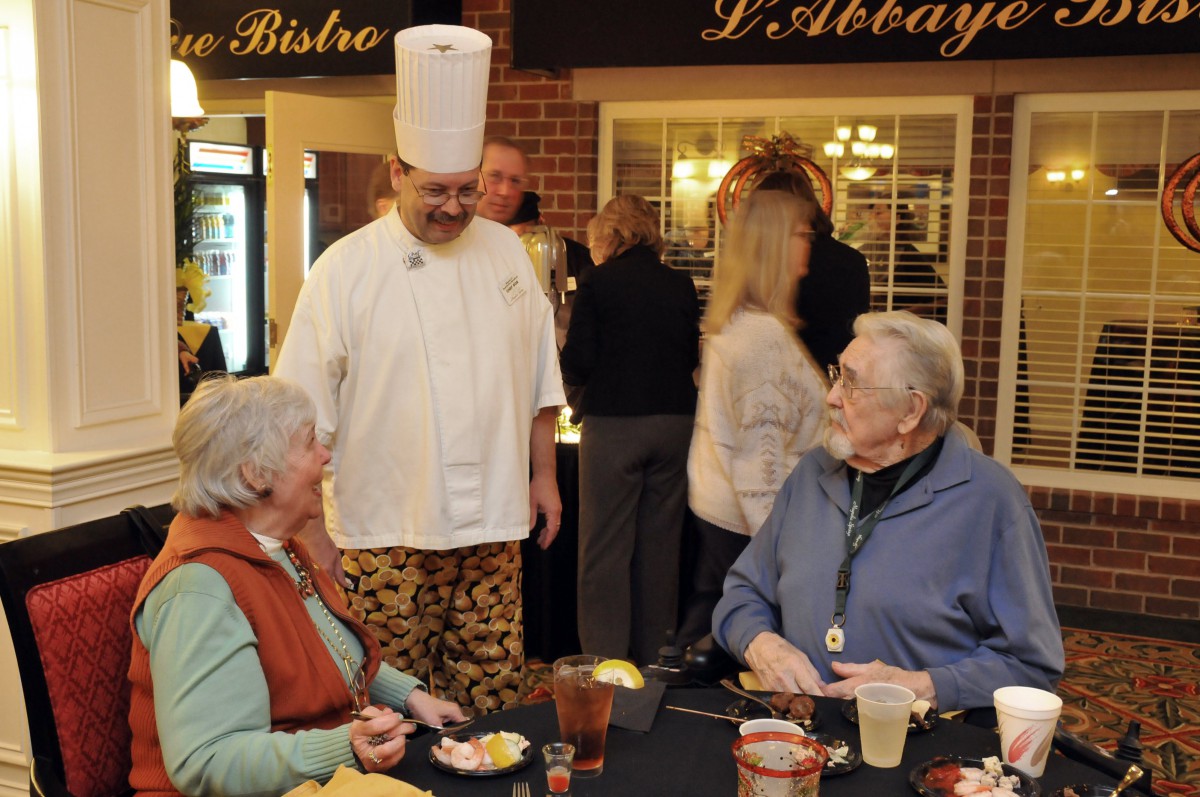 A chef interacts with diners in a restaurant setting.