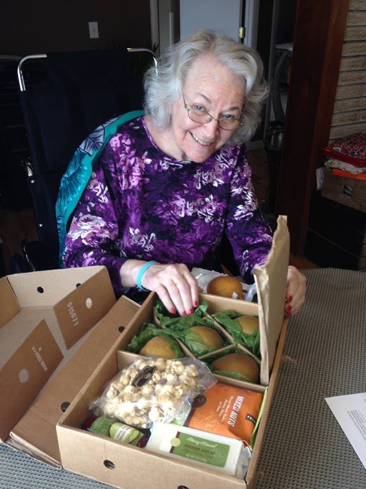 A smiling woman enjoying a gift box filled with fruit and snacks.