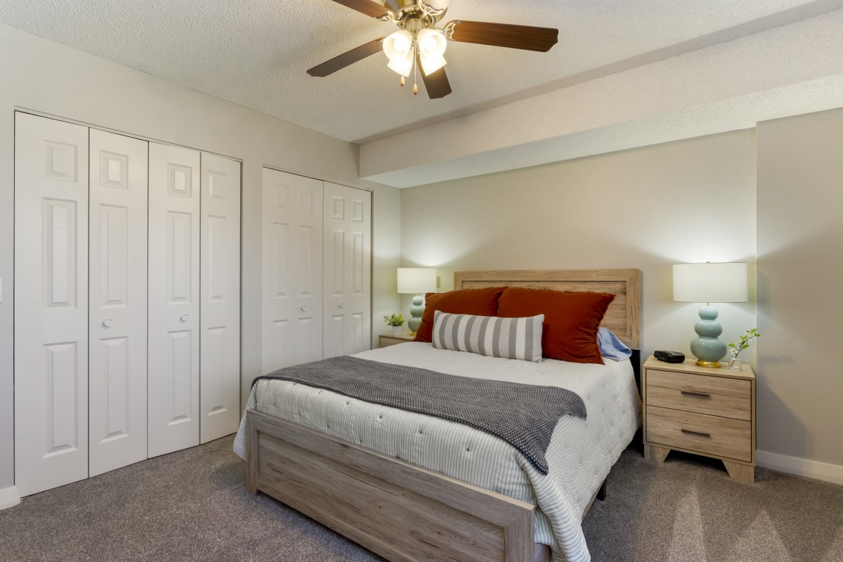 A cozy bedroom with a ceiling fan, featuring a neatly made bed and nightstands with lamps.